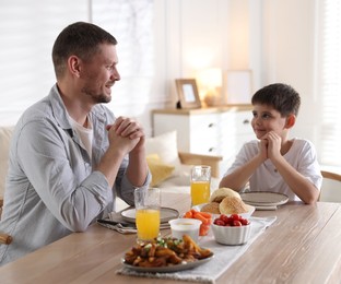 Photo of Father and son praying before dinner at table indoors
