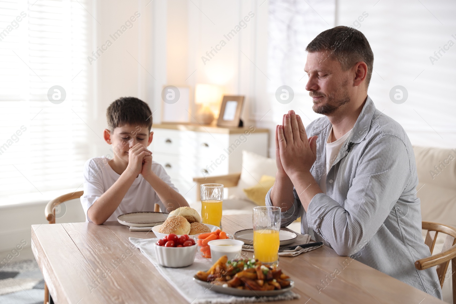 Father and son praying before dinner at table indoors Photo of Father and son praying before dinner at table indoors