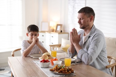 Photo of Father and son praying before dinner at table indoors