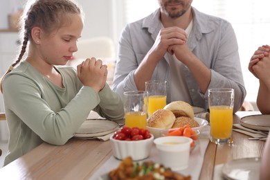 Photo of Family praying together before dinner at table indoors, closeup