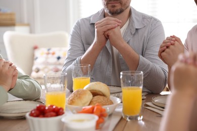 Photo of Family praying together before dinner at table indoors, closeup