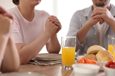 Photo of Family praying together before dinner at table indoors, closeup