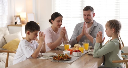 Photo of Family praying together before dinner at table indoors