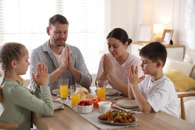 Photo of Family praying together before dinner at table indoors