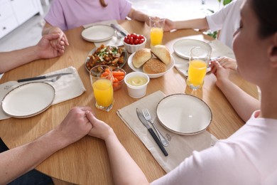 Photo of Family praying together before dinner at table indoors, closeup