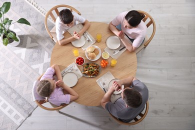 Photo of Family praying together before dinner at table indoors, above view