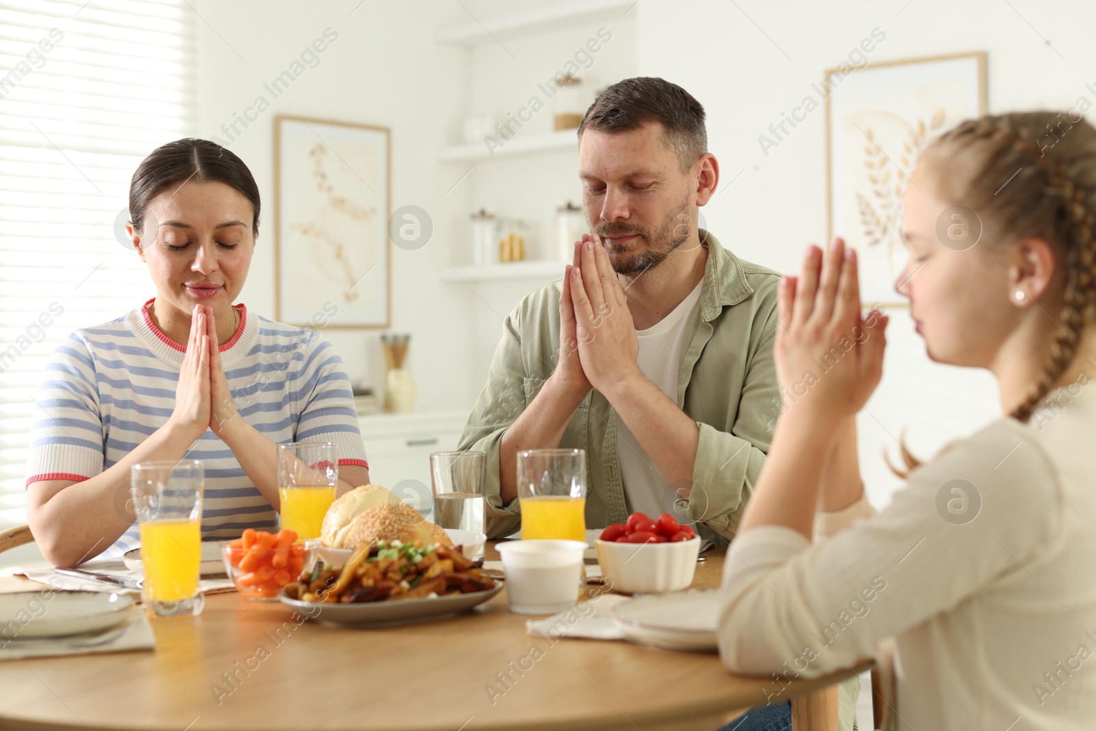 Family praying together before dinner at table indoors Photo of Family praying together before dinner at table indoors
