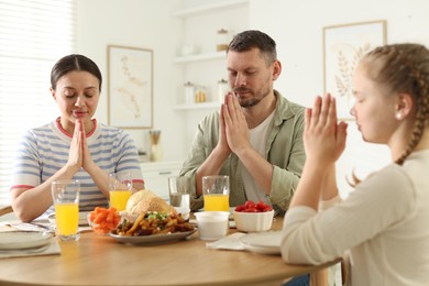 Photo of Family praying together before dinner at table indoors