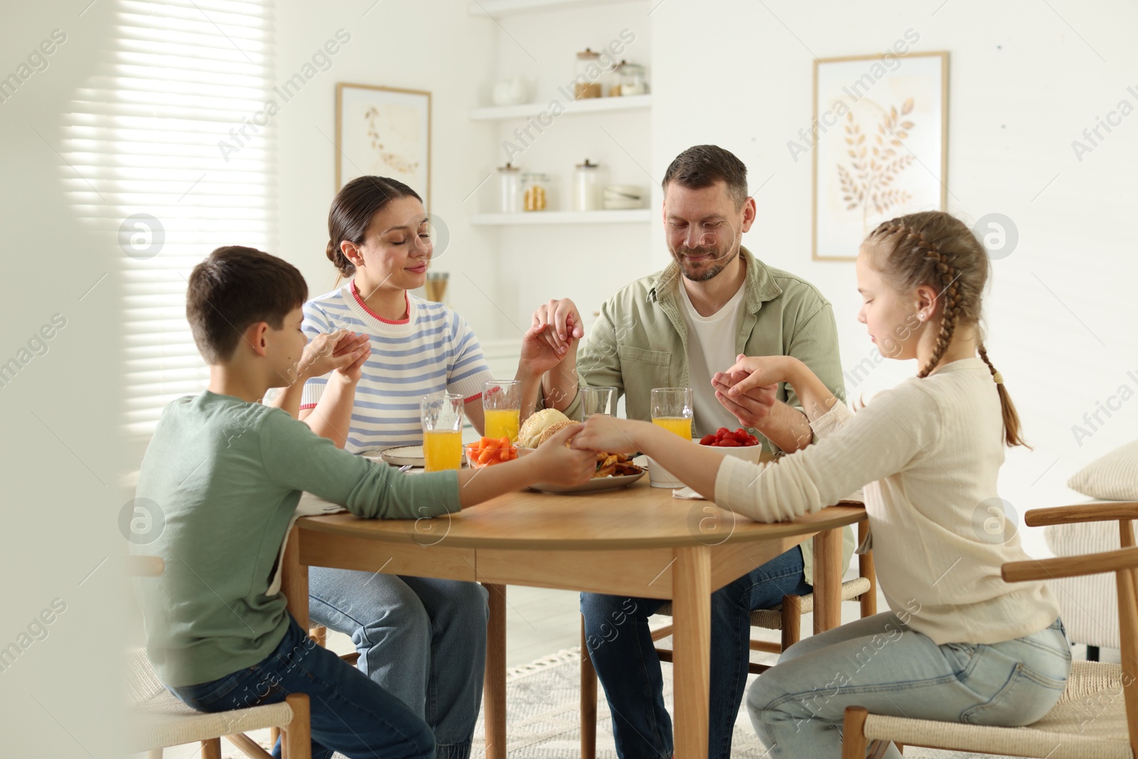 Photo of Family praying together before dinner at table indoors