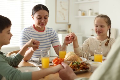 Photo of Mother and her children praying before dinner at table indoors