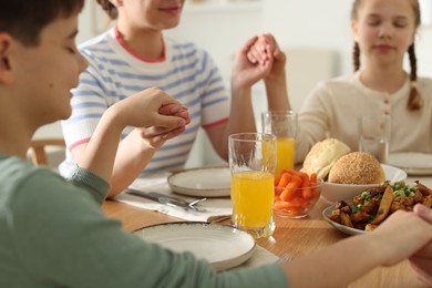 Photo of Mother and her children praying before dinner at table indoors, closeup