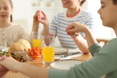 Photo of Mother and her children praying before dinner at table indoors, closeup