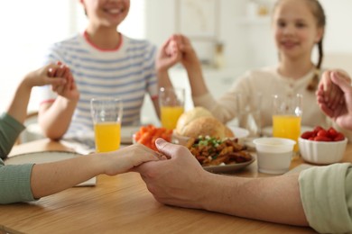 Photo of Family praying together before dinner at table indoors, closeup