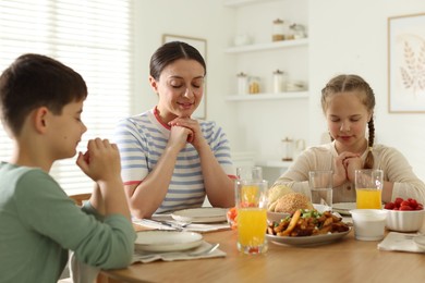 Photo of Family praying together before dinner at table indoors