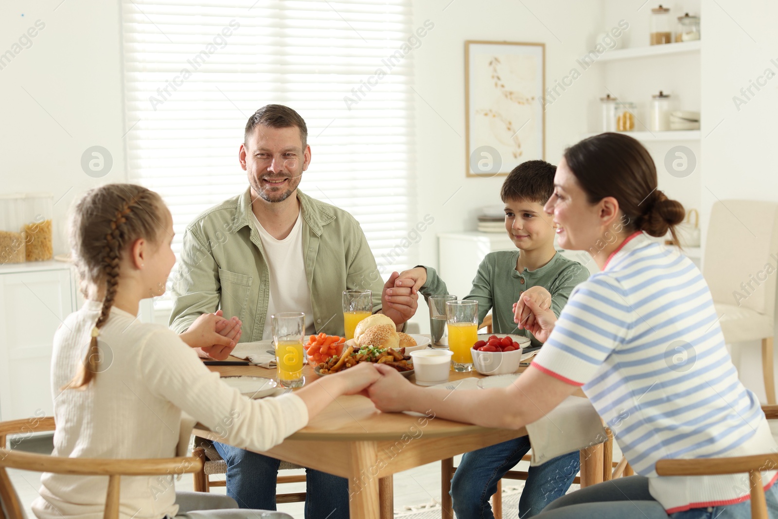 Family praying together before dinner at table indoors Photo of Family praying together before dinner at table indoors