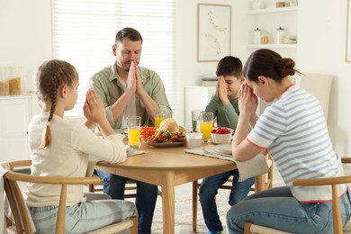 Photo of Family praying together before dinner at table indoors