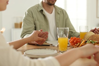 Photo of Family praying together before dinner at table indoors, closeup