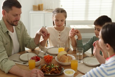 Photo of Family praying together before dinner at table indoors