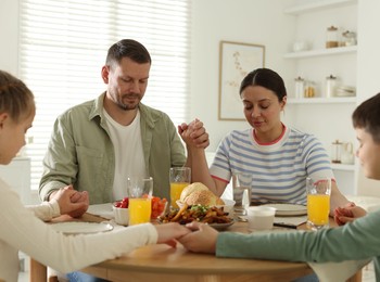 Photo of Family praying together before dinner at table indoors