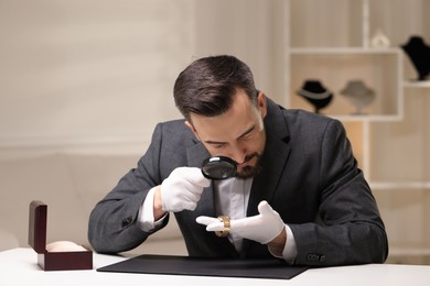 Photo of Appraiser evaluating luxury wristwatch at table indoors