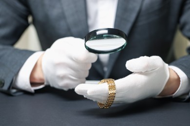 Photo of Appraiser evaluating luxury wristwatch at table indoors, closeup