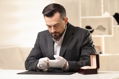 Photo of Appraiser working with luxury wristwatch at table indoors