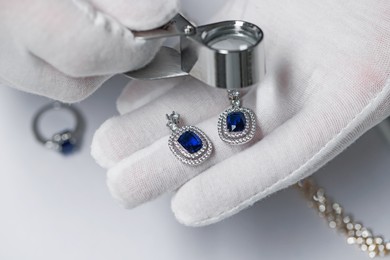 Photo of Appraiser with loupe evaluating luxury earrings at white table, closeup