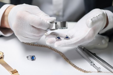 Photo of Appraiser with loupe evaluating luxury earrings at white table, closeup
