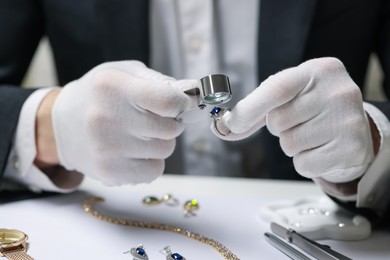 Photo of Appraiser with loupe evaluating luxury ring at white table, closeup