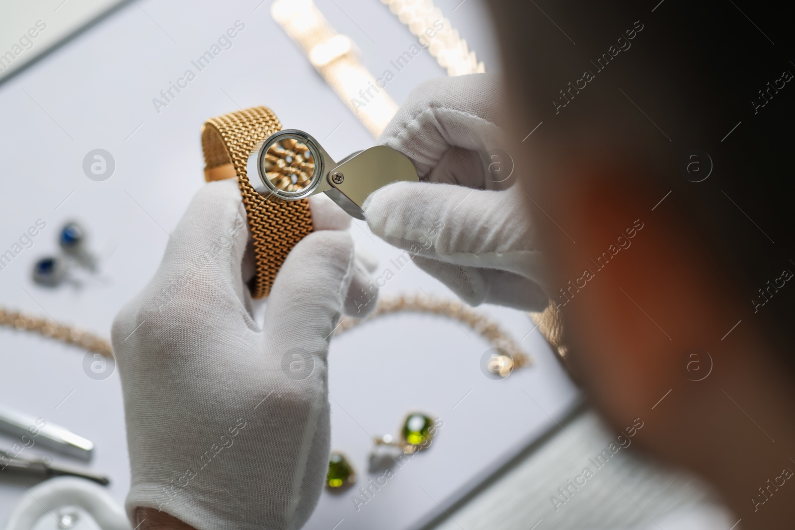 Appraiser with loupe evaluating luxury bracelet at table, above view Photo of Appraiser with loupe evaluating luxury bracelet at table, above view