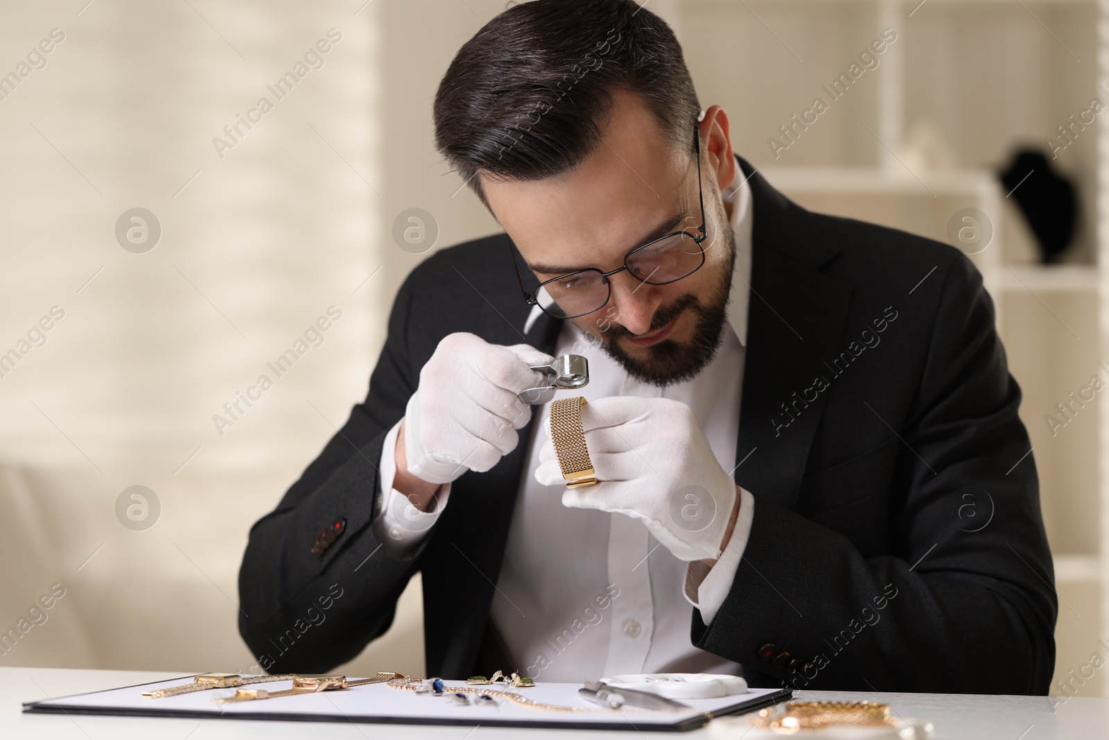 Appraiser with loupe evaluating luxury bracelet at table indoors Photo of Appraiser with loupe evaluating luxury bracelet at table indoors