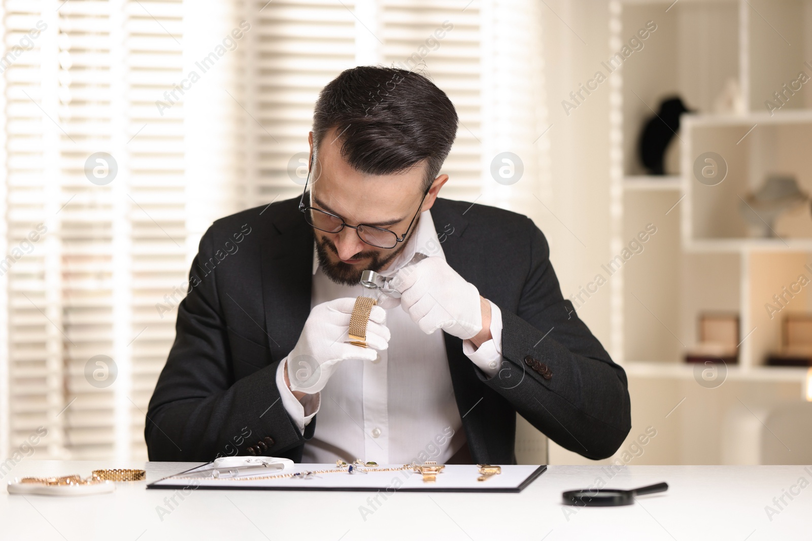 Appraiser with loupe evaluating luxury bracelet at table indoors Photo of Appraiser with loupe evaluating luxury bracelet at table indoors