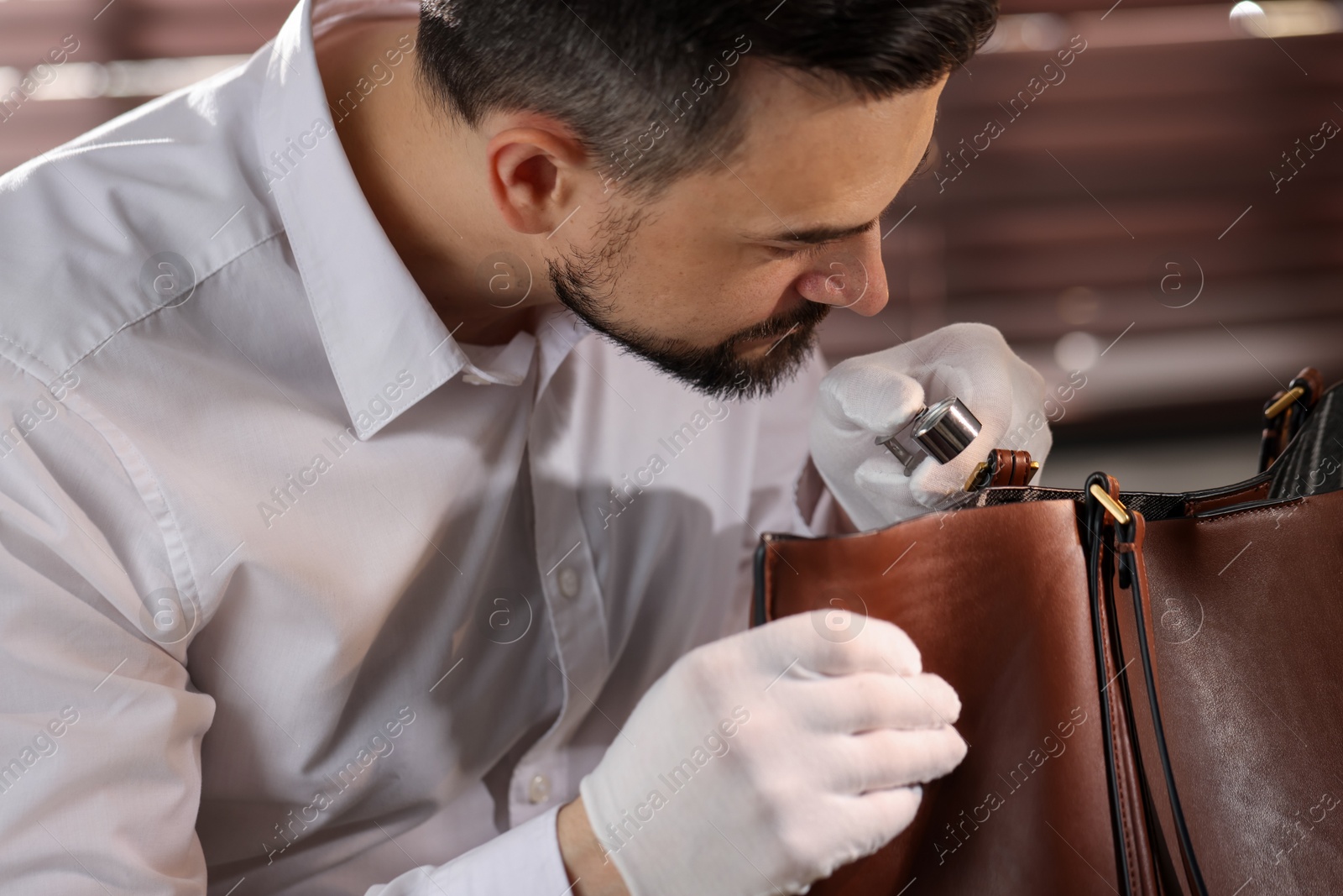 Appraiser with loupe evaluating leather bag indoors Photo of Appraiser with loupe evaluating leather bag indoors