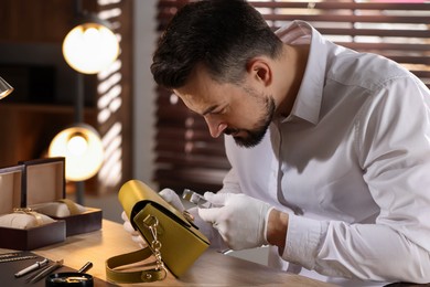 Photo of Appraiser with loupe evaluating leather bag at table indoors