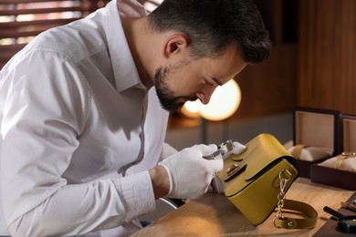 Photo of Appraiser with loupe evaluating leather bag at table indoors