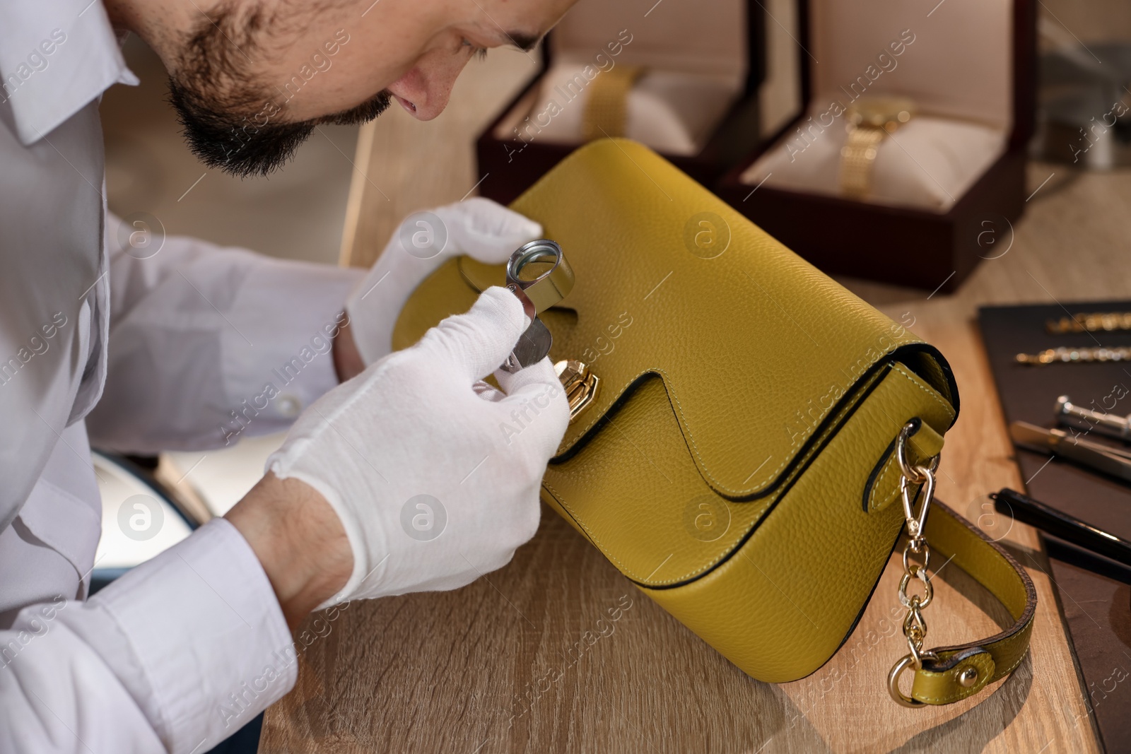 Appraiser with loupe evaluating leather bag at table indoors, closeup Photo of Appraiser with loupe evaluating leather bag at table indoors, closeup