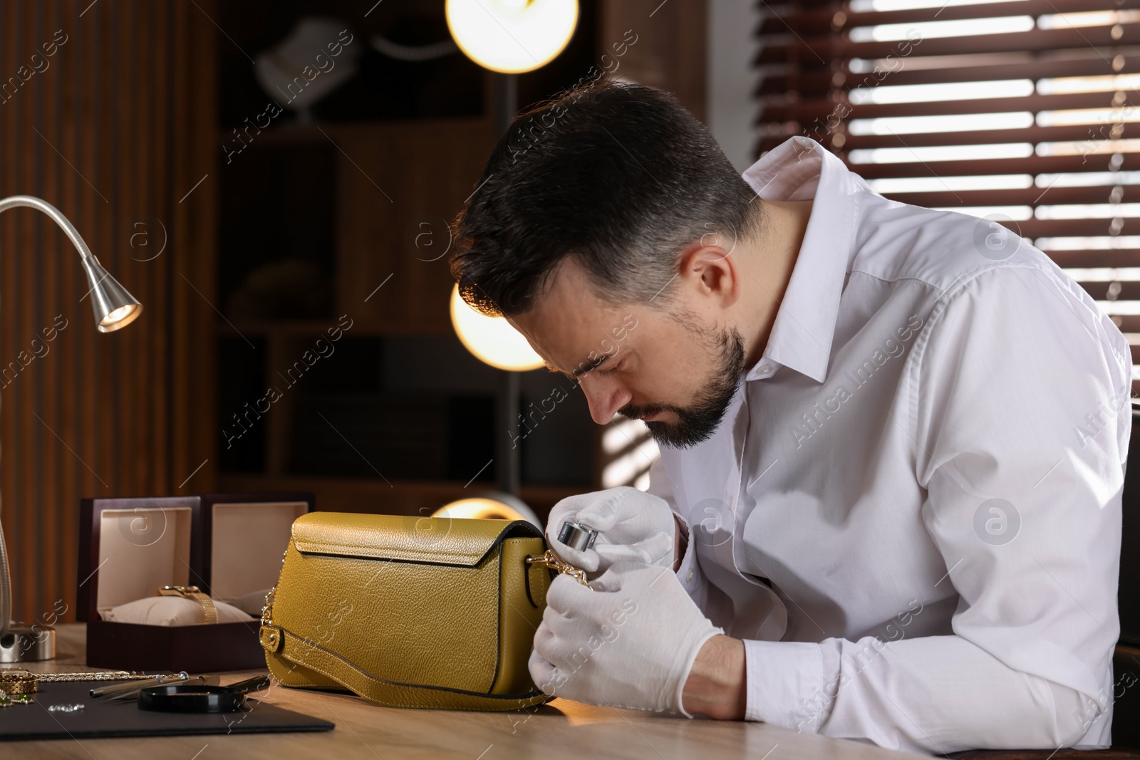 Appraiser with loupe evaluating leather bag at table indoors Photo of Appraiser with loupe evaluating leather bag at table indoors