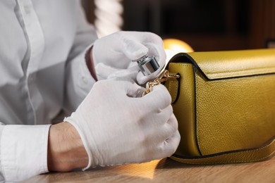 Photo of Appraiser with loupe evaluating leather bag at table indoors, closeup