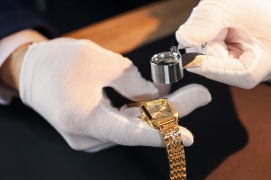 Photo of Appraiser with loupe evaluating luxury wristwatch at table, closeup