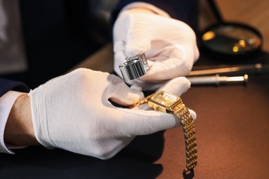 Photo of Appraiser with loupe evaluating luxury wristwatch at table, closeup
