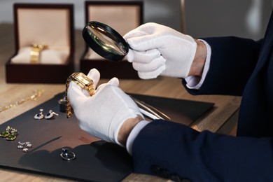 Photo of Appraiser with magnifying glass evaluating luxury wristwatch at table indoors, closeup