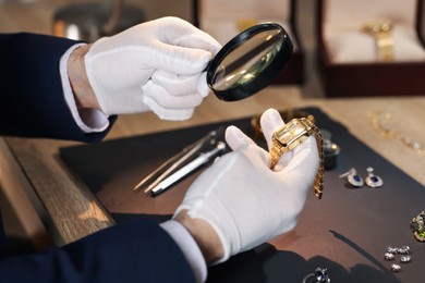 Photo of Appraiser with magnifying glass evaluating luxury wristwatch at table indoors, closeup