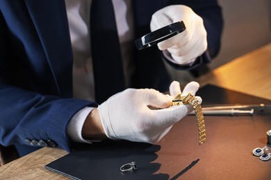 Photo of Appraiser with magnifying glass evaluating luxury wristwatch at table indoors, closeup
