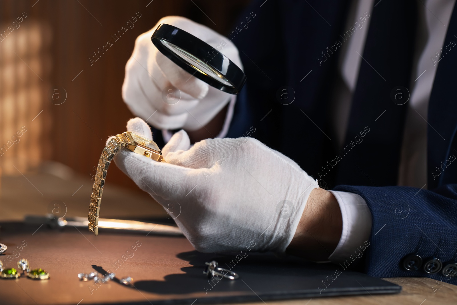 Appraiser with magnifying glass evaluating luxury wristwatch at table indoors, closeup Photo of Appraiser with magnifying glass evaluating luxury wristwatch at table indoors, closeup