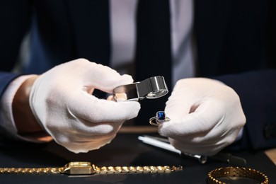 Photo of Appraiser with loupe evaluating ring at table indoors, closeup