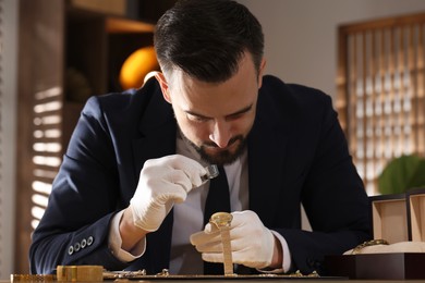 Photo of Appraiser with loupe evaluating luxury wristwatch at table indoors