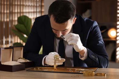 Photo of Appraiser with loupe evaluating luxury wristwatch at table indoors