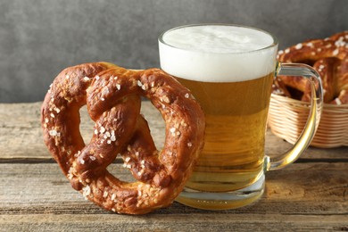 Photo of Tasty pretzel and glass of beer on wooden table against grey background, closeup