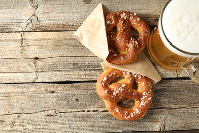 Photo of Tasty pretzels and glass of beer on wooden table, flat lay. Space for text
