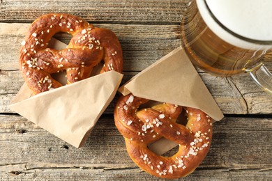 Photo of Tasty pretzels and glass of beer on wooden table, flat lay